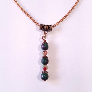 Puede incluir: Un collar de cadena de cobre con un colgante de piedra verde, roja y blanca.