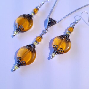 May include: A set of amber glass earrings and a necklace with silver chain and filigree accents. The earrings and necklace feature round amber glass beads with silver filigree accents.