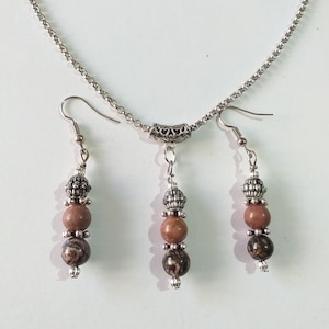May include: A silver chain necklace with a silver pendant and two matching earrings. The pendant and earrings each have three beads, two brown and one silver.