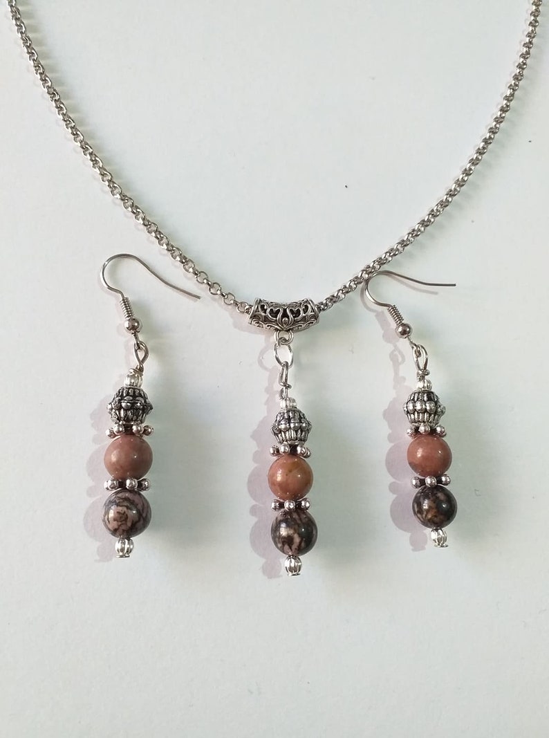 May include: A silver chain necklace with a silver pendant and two matching earrings. The pendant and earrings each have three beads, two brown and one silver.