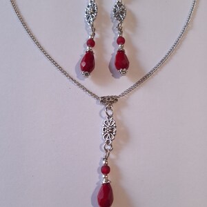 Puede incluir: Un collar de cadena de plata con un colgante de l&aacute;grima roja y un dije floral plateado. Aretes a juego con colgantes de l&aacute;grima roja y dijes florales plateados.