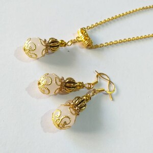 May include: A gold necklace and earrings set with a white pendant and matching earrings. The pendant and earrings feature a delicate gold design.