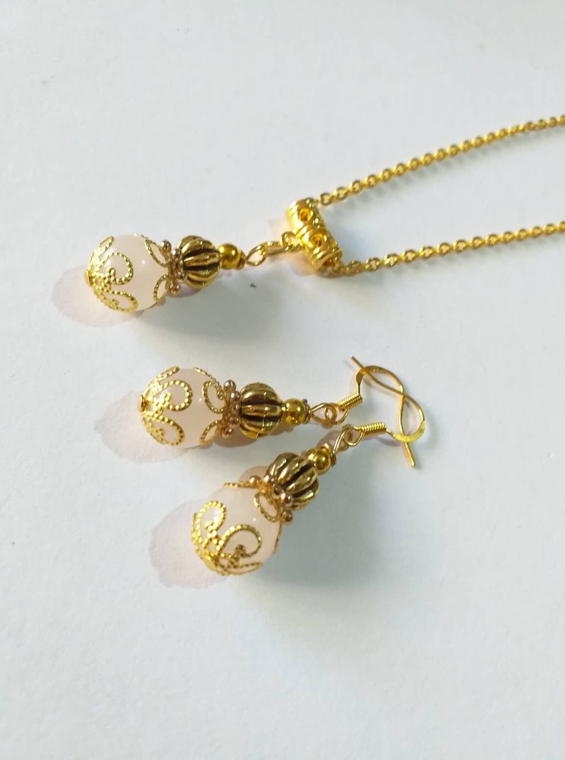 May include: A gold necklace and earrings set with a white pendant and matching earrings. The pendant and earrings feature a delicate gold design.