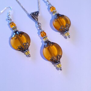 May include: A set of amber glass earrings and a necklace with silver filigree accents and yellow beads.
