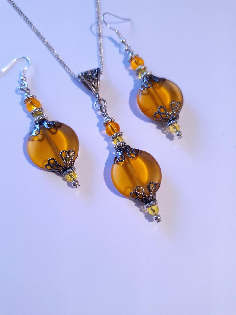 May include: A set of amber glass earrings and a necklace with silver filigree accents and yellow beads.