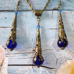 May include: A set of blue glass and gold tone drop earrings and necklace. The earrings and necklace feature a teardrop shaped pendant with a blue glass bead at the bottom.