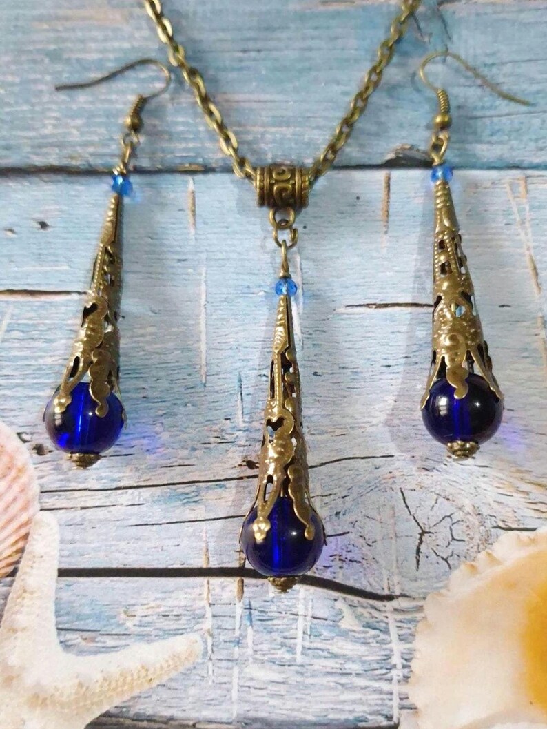 May include: A set of blue glass and gold tone drop earrings and necklace. The earrings and necklace feature a teardrop shaped pendant with a blue glass bead at the bottom.