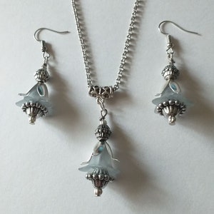 May include: A silver necklace and earrings set with a light blue flower pendant and matching earrings.