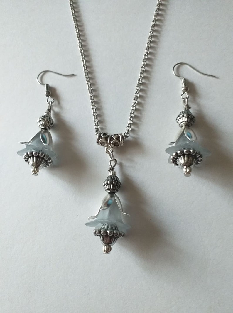 May include: A silver necklace and earrings set with a light blue flower pendant and matching earrings.