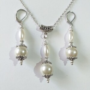 May include: A silver necklace and earrings set with white pearl beads and ornate silver accents.