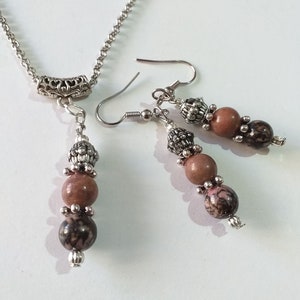 May include: A silver chain necklace with a silver pendant and three brown and black beads. Matching earrings with three brown and black beads and silver accents.