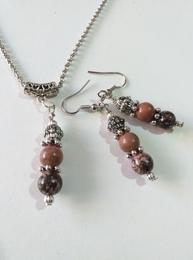 May include: A silver chain necklace with a silver pendant and three brown and black beads. Matching earrings with three brown and black beads and silver accents.