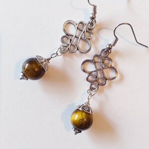 May include: A pair of silver earrings with a knotted design and a round tiger's eye stone dangle.