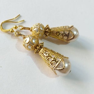 May include: A pair of gold filigree earrings with white pearl drops. The earrings have a delicate, intricate design and are perfect for adding a touch of elegance to any outfit.