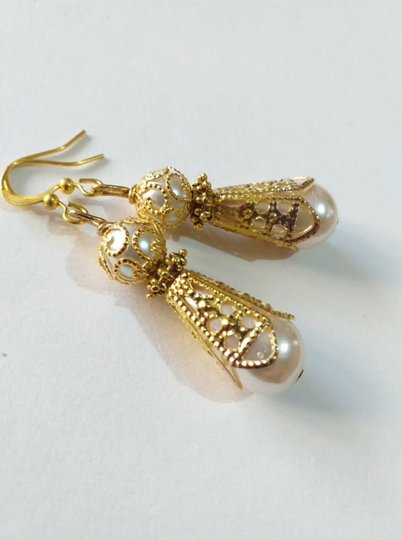 May include: A pair of gold filigree earrings with white pearl drops. The earrings have a delicate, intricate design and are perfect for adding a touch of elegance to any outfit.