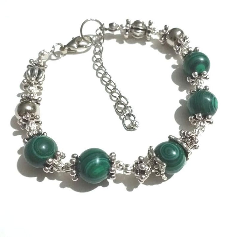 May include: A silver bracelet with green malachite beads and silver accents. The bracelet has a lobster clasp closure.