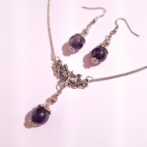Puede incluir: Un collar de plata con un delicado colgante floral y una piedra preciosa de amatista colgante. Pendientes de amatista a juego con ganchos de plata.
