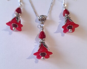 Könnte beinhalten: Eine Halskette mit Anhänger und passenden Ohrringen in Form einer roten Blume. Anhänger und Ohrringe zeigen eine rote Blume mit silbernen Akzenten.