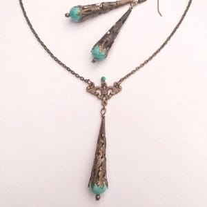 Puede incluir: Un conjunto de collar y pendientes de color turquesa y bronce con un delicado dise&ntilde;o de filigrana. El colgante tiene forma de l&aacute;grima con una piedra turquesa en la parte inferior. Los pendientes tambi&eacute;n tienen forma de l&aacute;grima con piedras turquesas en la parte inferior.
