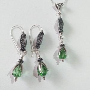 May include: A silver necklace and earrings set with green crystal teardrop pendants and ornate silver beads.
