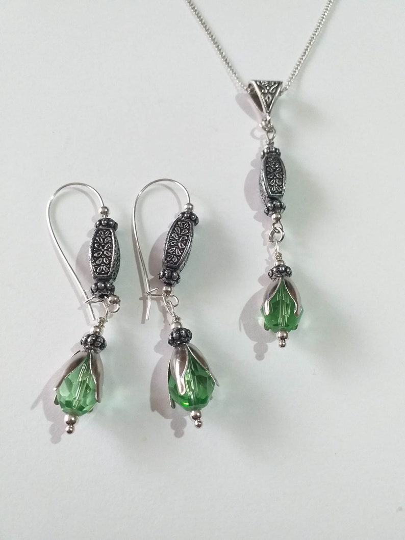 May include: A silver necklace and earrings set with green crystal teardrop pendants and ornate silver beads.