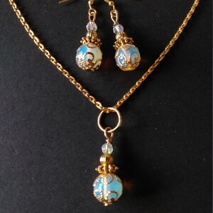 May include: A gold chain necklace with a pendant and matching earrings. The pendant and earrings feature a blue and white opal-like stone with a gold filigree design.