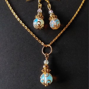May include: A gold chain necklace with a pendant and matching earrings. The pendant and earrings feature a blue and white opal-like stone with gold filigree detailing.