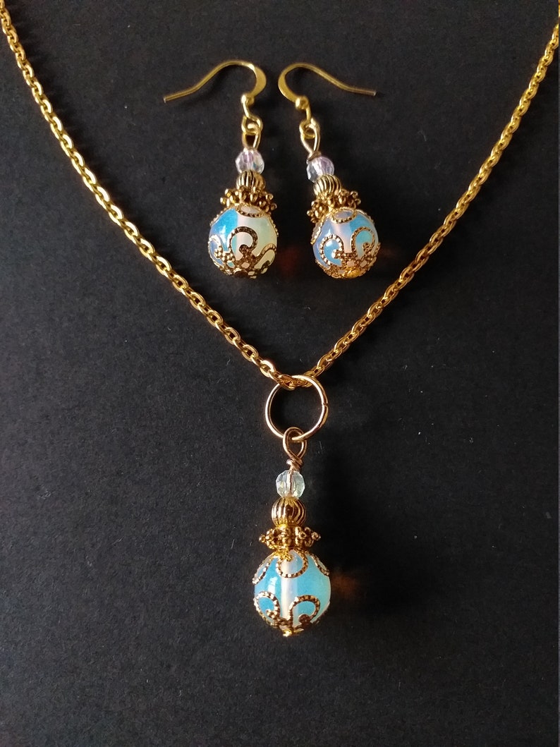 May include: A gold chain necklace with a pendant and matching earrings. The pendant and earrings feature a blue and white opal-like stone with gold filigree detailing.