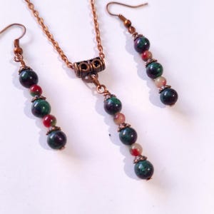 Puede incluir: Un collar de cadena de cobre y pendientes a juego con un diseño de cuentas de piedra verde, roja y blanca.