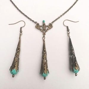 Puede incluir: Un conjunto de collar y pendientes de turquesa y bronce. El collar presenta un delicado colgante con una piedra turquesa y detalles intrincados en bronce. Los pendientes son largos y colgantes, tambi&eacute;n con piedras turquesa y acentos de bronce.