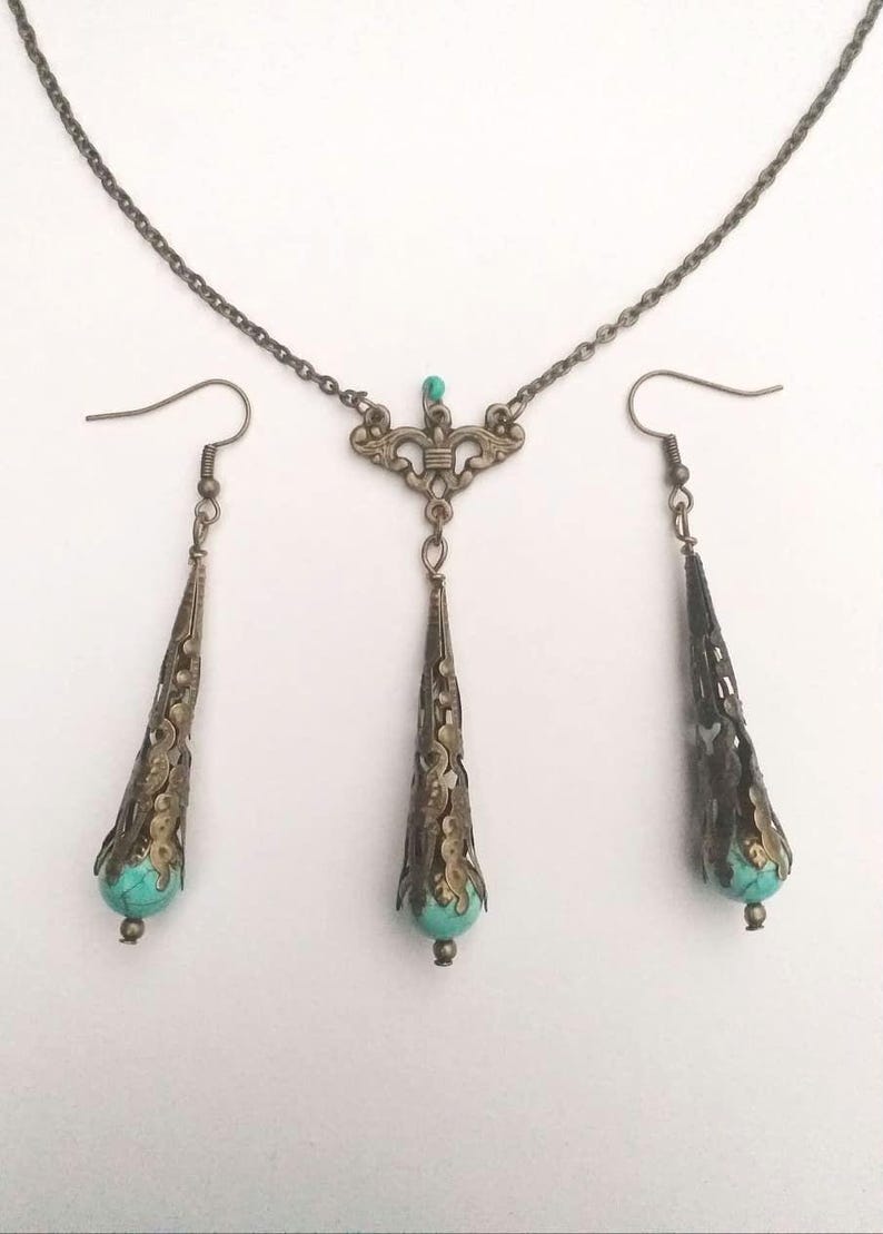 Puede incluir: Un conjunto de collar y pendientes de turquesa y bronce. El collar presenta un delicado colgante con una piedra turquesa y detalles intrincados en bronce. Los pendientes son largos y colgantes, tambi&eacute;n con piedras turquesa y acentos de bronce.