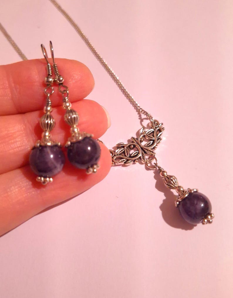 Puede incluir: Un collar y pendientes de plata con cuentas de piedra preciosa amatista. El collar presenta un delicado colgante de plata con un dise&ntilde;o floral. Los pendientes son pendientes de gota simples con cuentas de amatista.