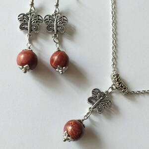 May include: A silver necklace and earrings set with a red stone and butterfly charm.