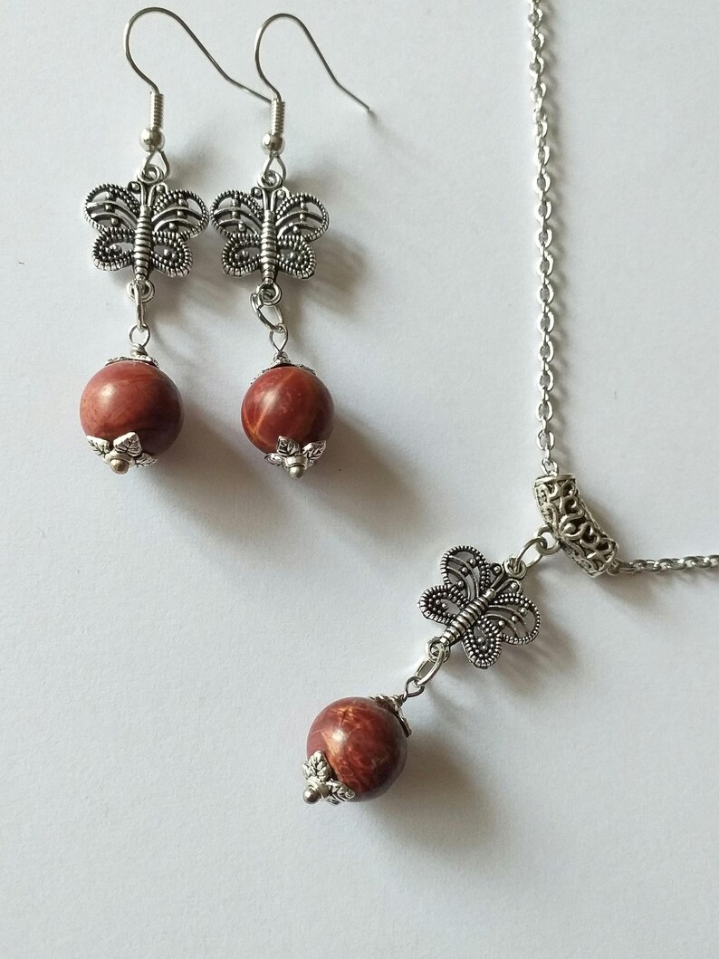 May include: A silver necklace and earrings set with a red stone and butterfly charm.
