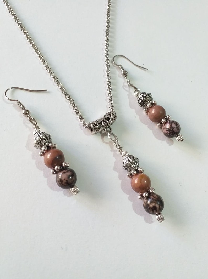 May include: A silver chain necklace with a silver pendant and three brown and black beads. Matching earrings with three brown and black beads hang from silver hooks.