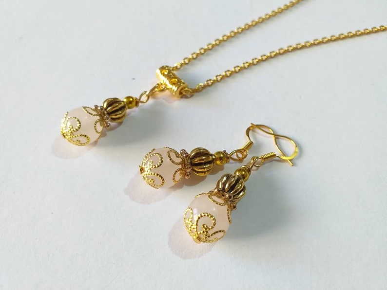 May include: A delicate gold necklace and earrings set with a pink glass bead accented with gold filigree.