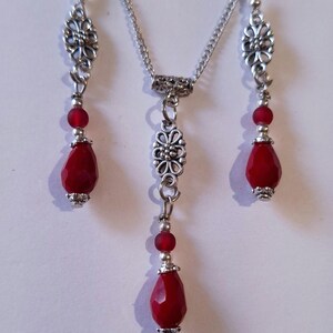 Puede incluir: Un collar y pendientes de plata con cuentas rojas en forma de l&aacute;grima y detalles florales.