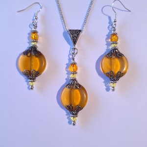 May include: A set of amber glass earrings and a necklace with silver accents. The earrings and necklace feature a round, teardrop-shaped bead with a filigree design.