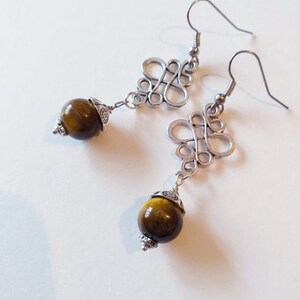 May include: A pair of silver earrings with a knotted design and a round tiger's eye stone pendant.