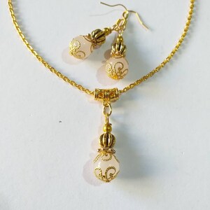 May include: A gold chain necklace with a white pendant and matching earrings. The pendant and earrings feature a white stone with gold filigree designs.