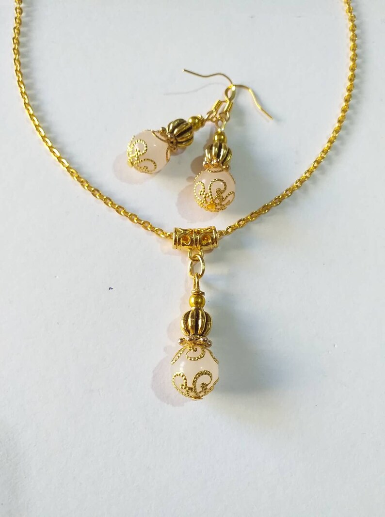 May include: A gold chain necklace with a white pendant and matching earrings. The pendant and earrings feature a white stone with gold filigree designs.
