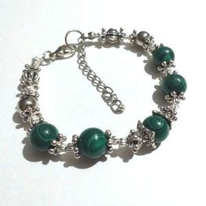 May include: A silver bracelet with green malachite beads and silver accents. The bracelet has a lobster clasp closure.