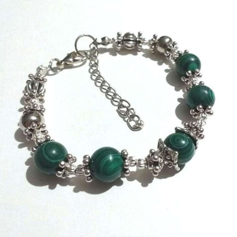 May include: A silver bracelet with green malachite beads and silver accents. The bracelet has a lobster clasp closure.