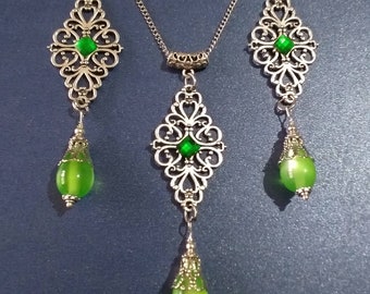 Puede incluir: Un collar y pendientes de plata con detalles de piedras preciosas verdes. El collar presenta un colgante con un diseño de filigrana y una piedra verde en forma de lágrima. Los pendientes tienen un diseño similar con una piedra verde en forma de lágrima más pequeña.