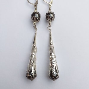 May include: A pair of silver dangle earrings with black beads and intricate filigree designs.