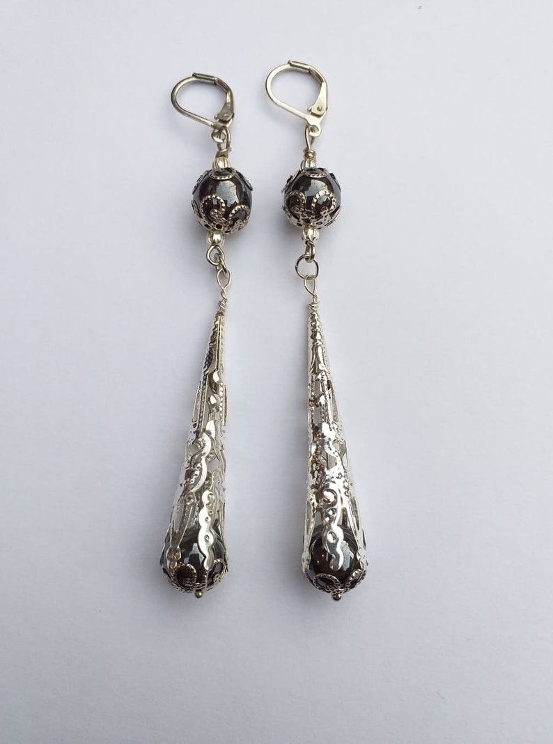 May include: A pair of silver dangle earrings with black beads and intricate filigree designs.