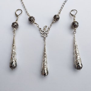 May include: A silver necklace and earrings set with black beads and a delicate butterfly pendant. The necklace and earrings feature a teardrop design with intricate details.