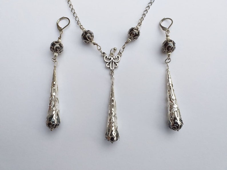 May include: A silver necklace and earrings set with black beads and a delicate butterfly pendant. The necklace and earrings feature a teardrop design with intricate details.