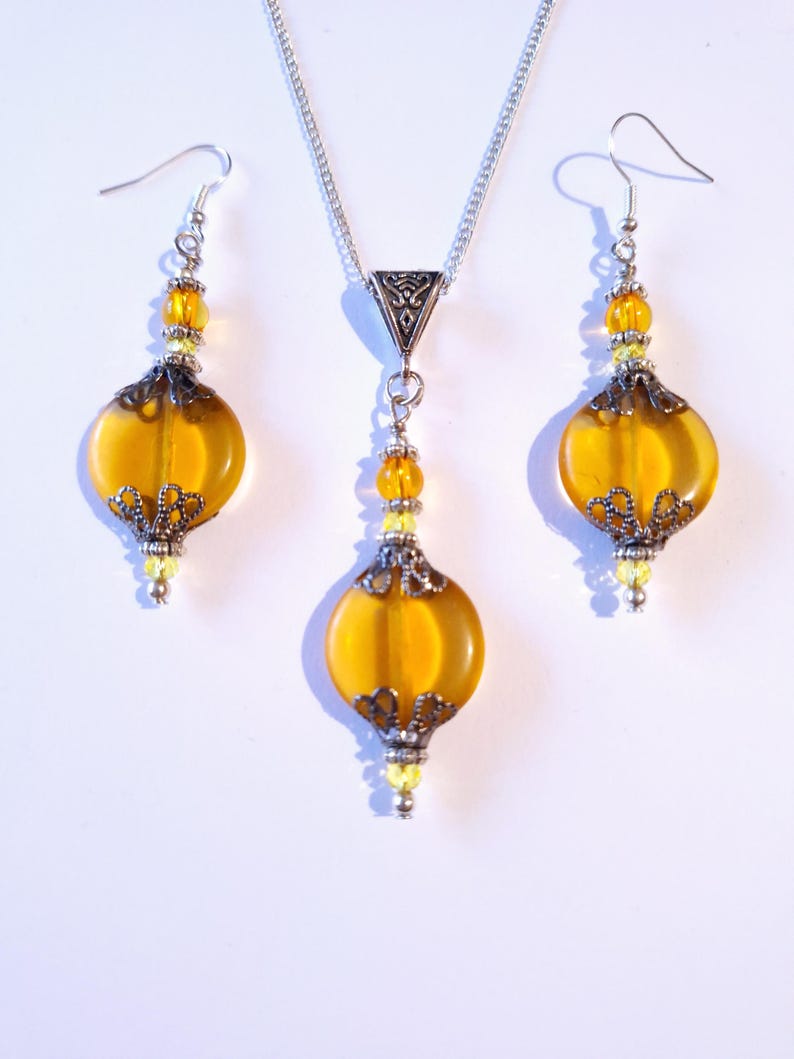 May include: A silver necklace and earrings set with amber glass beads and silver filigree accents.