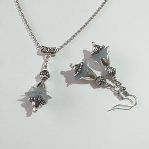 May include: A silver necklace and earrings set with a delicate flower design. The necklace features a silver chain with a flower pendant, while the earrings have a flower dangle with a silver hook.